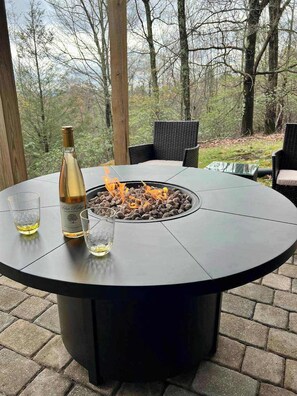 Ein runder Gartentisch mit integriertem Feuerkorb, umgeben von Korbstühlen.