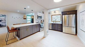 Una cocina moderna con una isla central, armarios oscuros, electrodomésticos de acero inoxidable e iluminación colgante.