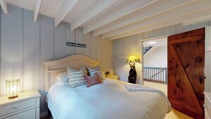 Un dormitorio con cama, mesita de noche, lámpara, puerta de madera y un cartel en la pared.
