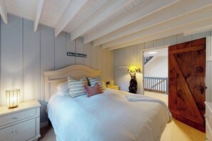 A bedroom with a bed, a nightstand, a lamp, a wooden door, and a sign on the wall.