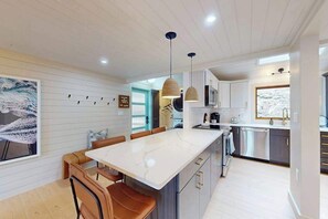 Une cuisine moderne dotée d’un îlot central, de luminaires suspendus et offrant une vue sur l’extérieur.
