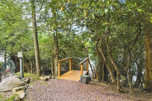 Un pont en bois mène à une petite construction en bois, elle-même entourée d’arbres.