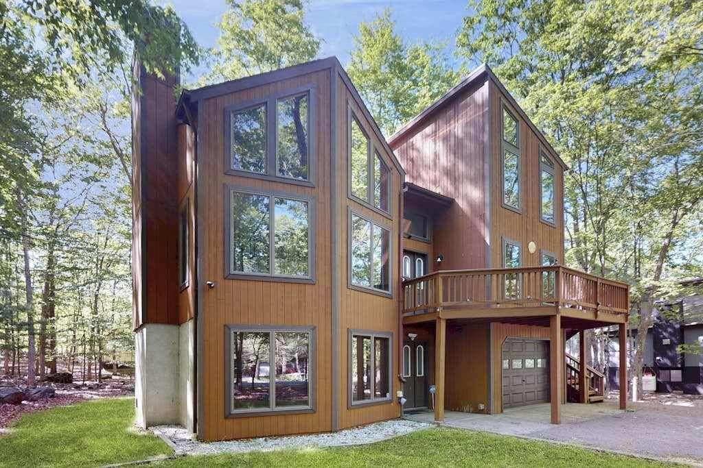 A multi-story wooden cabin with large windows, a deck, and a garage.