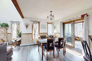 Un espace repas comprenant une table et des chaises, un lustre et une vue sur l’extérieur, visible à travers une porte vitrée.