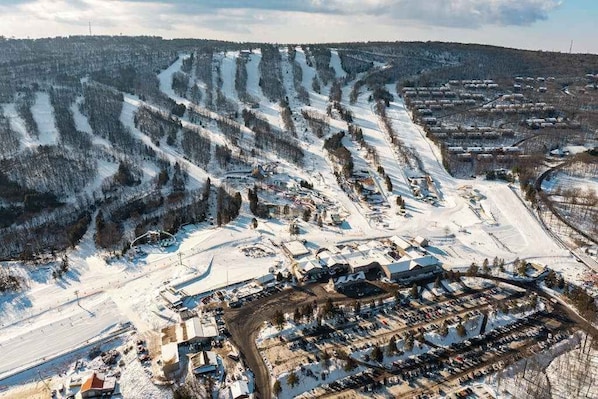 Ett flygbildsbild av ett snötäckt landskap med en parkeringsplats, byggnader och en skidbacke.