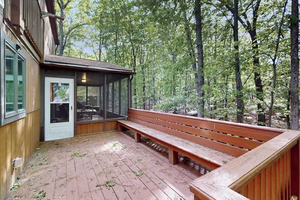Una terraza de madera con un banco, un ventanal de vidrio y vistas a un bosque.