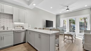 A modern kitchen with grey cabinets, a central island, and a dining area with wicker furniture. - Henderson Beach Resort Lofts 104- Poolside Paradise (Destin)