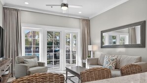A spacious living area with a large window, a ceiling fan, and a marble coffee table. - Henderson Beach Resort Lofts 104- Poolside Paradise (Destin)