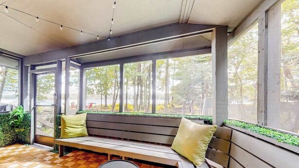 A modern interior with a wooden bench, a small round table, and large windows offering a view of trees.