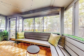 Un intérieur moderne avec un banc en bois, une petite table ronde et de grandes fenêtres donnant sur la forêt.