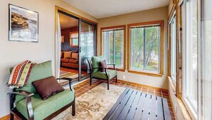 A sunlit room with a sofa, chairs, and a view through large windows.