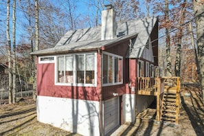 Eine kleine Holzhütte mit rotem und weißem Anstrich, einem Schornstein, einer Garage und einer Holzterrasse.