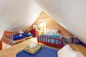 Ein gemütliches Schlafzimmer im Dachgeschoss mit zwei Betten, einer Holzbalkendecke und einem Fenster mit Tageslicht.