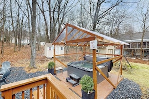 A hot tub under a wooden pergola with a deck, surrounded by trees and a house in the background. - Lakeside Chalet with Hot Tub, Fire Pit & Game Room (Blakeslee)