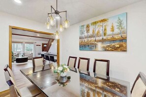 A dining area with a long table, chairs, a chandelier, and a painting of a landscape. - Lakeside Chalet with Hot Tub, Fire Pit & Game Room (Blakeslee)