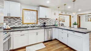 A modern kitchen with white cabinets, a tiled backsplash, and a wooden floor. - Lakeside Chalet with Hot Tub, Fire Pit & Game Room (Blakeslee)