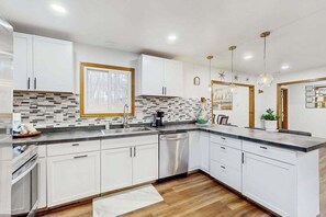 A modern kitchen with white cabinets, a tiled backsplash, and a wooden floor. - Lakeside Chalet with Hot Tub, Fire Pit & Game Room (Blakeslee)