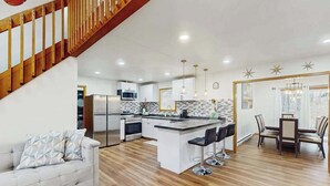 A modern kitchen with a central island, bar stools, and a dining area with a table and chairs. - Lakeside Chalet with Hot Tub, Fire Pit & Game Room (Blakeslee)