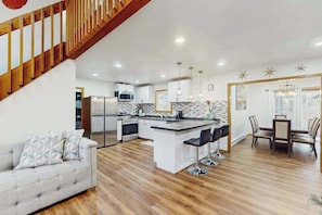 A modern kitchen with a central island, bar stools, and a dining area with a table and chairs. - Lakeside Chalet with Hot Tub, Fire Pit & Game Room (Blakeslee)