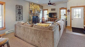 A living room with a stone fireplace, a large sofa, a television, and a ceiling fan. - Cozy Home Near Waterpark - Hot Tub and Deck (Tannersville)