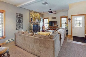 A living room with a stone fireplace, a large sofa, a television, and a ceiling fan. - Cozy Home Near Waterpark - Hot Tub and Deck (Tannersville)