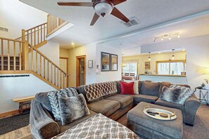 Ein Wohnzimmer mit einer Holztreppe, einem Deckenventilator, einer Sofagarnitur und einem Essbereich.