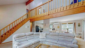 Ein Wohnzimmer mit Ecksofa, einer Holztreppe und einer Küche im Hintergrund.