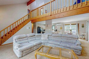 A living room with a sectional sofa, a wooden staircase, and a kitchen in the background. - Dog-Friendly Home with Hot Tub, Decks & Pool Table (Albrightsville)