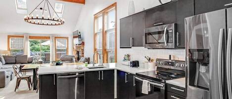 A modern kitchen with stainless steel appliances, a central island, and a dining area with a sofa and table.