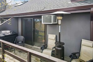 Eine überdachte Terrasse im Freien mit Grill, zwei Stühlen und einer Klimaanlage.