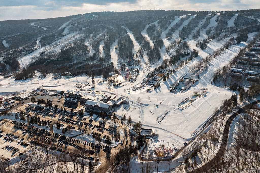 Ein schneebedecktes Skigebiet mit mehreren Gebäuden, Parkplätzen und Skipisten.