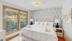 Un dormitorio con una cama grande, dos mesitas de noche con lámparas, una lámpara de techo, una ventana con vistas y una pared con diseño.