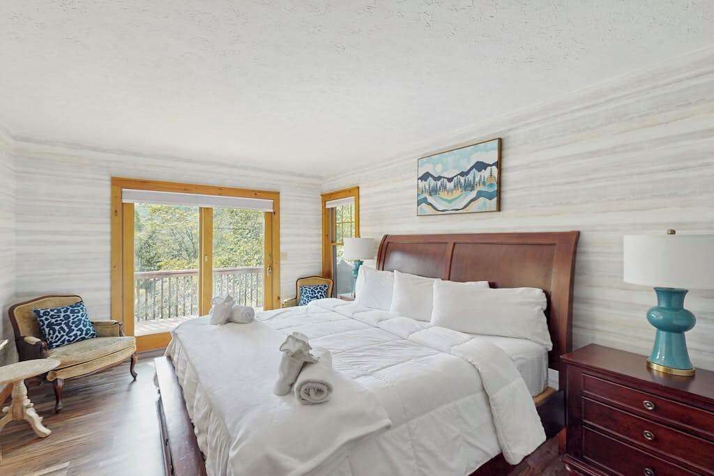 Habitación de hotel con una cama grande, cabecera de madera, un cuadro en la pared y vistas al exterior a través de las ventanas.