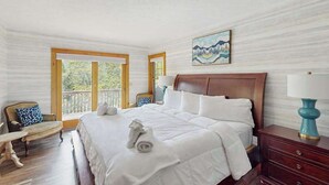 Habitación de hotel con una cama grande, cabecera de madera, un cuadro en la pared y vistas al exterior a través de las ventanas.
