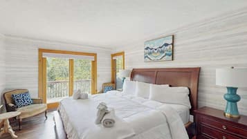 Habitación de hotel con una cama grande, cabecera de madera, un cuadro en la pared y vistas al exterior a través de las ventanas.