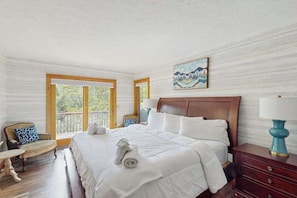 Ein Hotelzimmer mit einem großen Bett, einem hölzernen Kopfteil, einem Bild an der Wand und Blick ins Freie durch die Fenster.