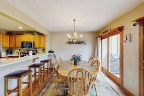 A dining area with a wooden table and chairs, a chandelier, and a kitchen with wooden cabinets and a microwave. - Cozy Home with Wood Fireplace and Views (Tannersville)