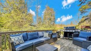 An outdoor deck with wicker furniture, a grill, and a view of trees and sky. - Spacious House with Hot Tub & Game Room (Long Pond)