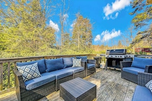 An outdoor deck with wicker furniture, a grill, and a view of trees and sky. - Spacious House with Hot Tub Game Room and Firepit (Long Pond)