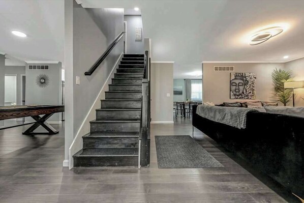 A modern interior with a staircase, a pool table, a sofa, and a Buddha painting. - Spacious House with Hot Tub Game Room and Firepit (Long Pond)