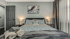 A bedroom with a bed, two bedside lamps, a door, and a wall art piece. - Spacious House with Hot Tub & Game Room (Long Pond)