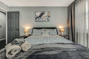 A bedroom with a bed, two bedside lamps, a door, and a wall art piece. - Spacious House with Hot Tub Game Room and Firepit (Long Pond)