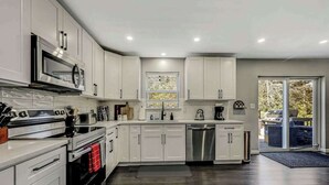 A modern kitchen with white cabinets, stainless steel appliances, and a large window. - Spacious House with Hot Tub & Game Room (Long Pond)