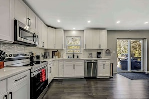 A modern kitchen with white cabinets, stainless steel appliances, and a large window. - Spacious House with Hot Tub Game Room and Firepit (Long Pond)