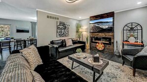 A modern living room with a fireplace, a dining area, and a kitchen in the background. - Spacious House with Hot Tub & Game Room (Long Pond)