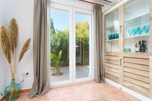 Ein Zimmer mit einer Schiebetür zum Garten, einer Glasvase mit getrockneten Pflanzen und einem Holzkabinett mit Gläsern.
