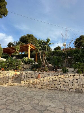 Un muro de piedra, una pérgola de madera y diversas plantas.