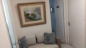 Une pièce avec un canapé, un tableau encadré, une porte portant l’inscription « CHAMBRE », et un sol carrelé.