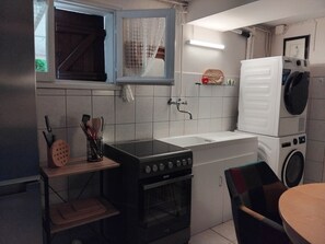 Une cuisine compacte Ă©quipĂ©e dâune cuisiniĂšre Ă gaz, dâun four encastrĂ©, dâun Ă©vier, dâun lave-linge et dâune fenĂȘtre avec un rideau.