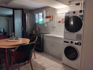 A compact kitchen with a washing machine, a dining table with chairs, and a refrigerator.
